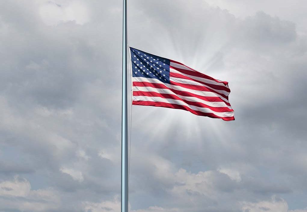 Half mast American flag concept with the symbol of the United States flying at low level on the flagpole or staff on a cloudy day with a sun glow as an icon of honor respect and mourning for fallen heros.